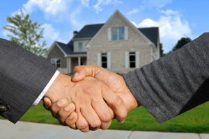 Hands of two men shaking hands in front of a house