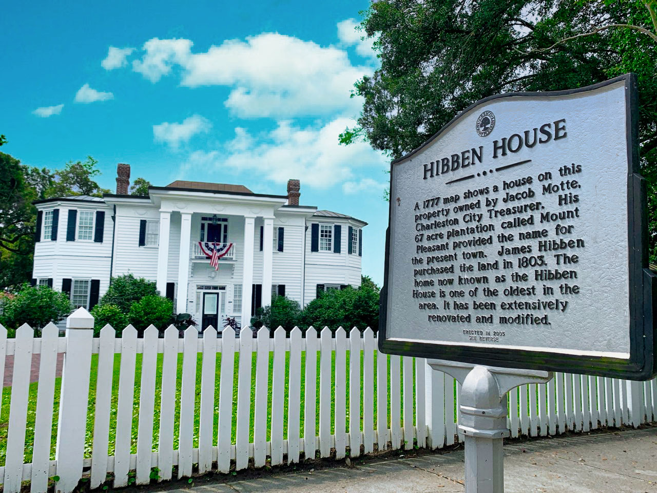Hibben House in the Old Village of Mt. Pleasant, SC. White 2-story house with columned portico and black shutters behind a white picket fence with historic marker.