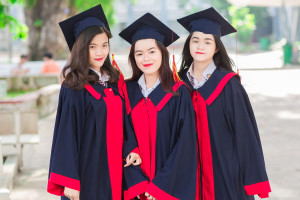 three women in black caps and gown with red scarfs at a college student graduation