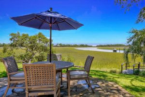 Teak table and chairs and umbrella outside on the marsh with a boat in the water in the distance on Kiawah Island, SC