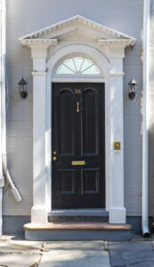 Black front door to a historic house with fanlight above and detailed white molding around.