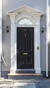 Black front door to a historic house with fanlight above and detailed white molding around.