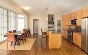 Interior of a Charleston contemporary style house.Great room with kitchen to the right, kitchen island in the center, and dining table to the left. Cabinets are blonde wood; floor is medium hardwood. 