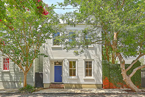 Charleston single family home exterior. White 2-story house with blue door surrounded by trees.