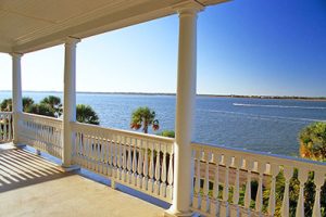 View of the Ashley River from a white porch with columns and rails on a waterfront Charleston home. 