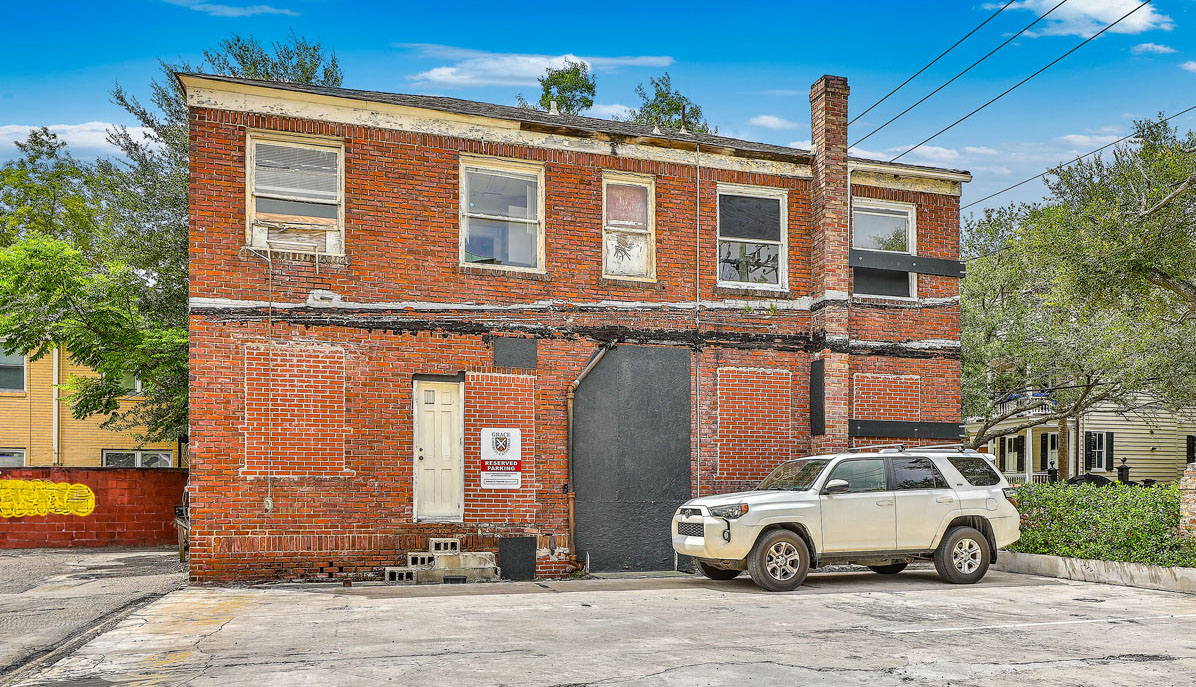 115 Wentworth Street. Vacant brick office building with boarded up windows from the side with parking lot next to it.